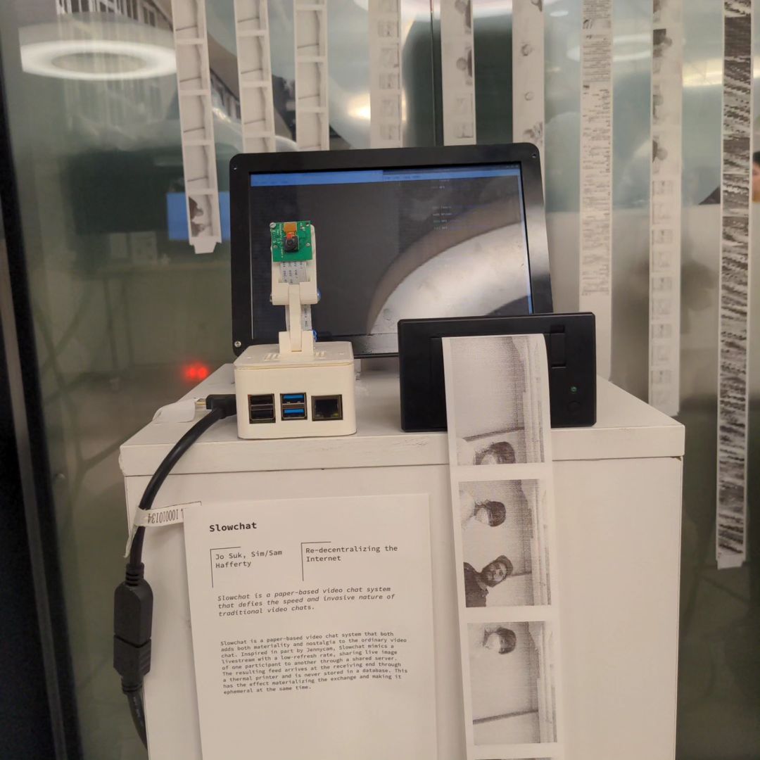 Photo of a robotic mechanism in wooden casing with a small printer atop and a small paper shredder below, paper coming out of the printer is fed into the shredder and shown shredded below.